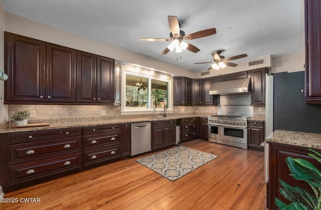 kitchen featuring light hardwood / wood-style flooring, appliances with stainless steel finishes, light stone countertops, decorative backsplash, and wall chimney exhaust hood