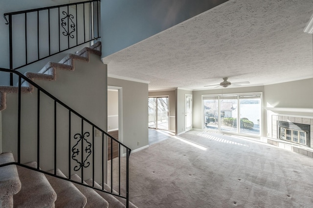 living room with crown molding, light carpet, a textured ceiling, ceiling fan, and a tiled fireplace