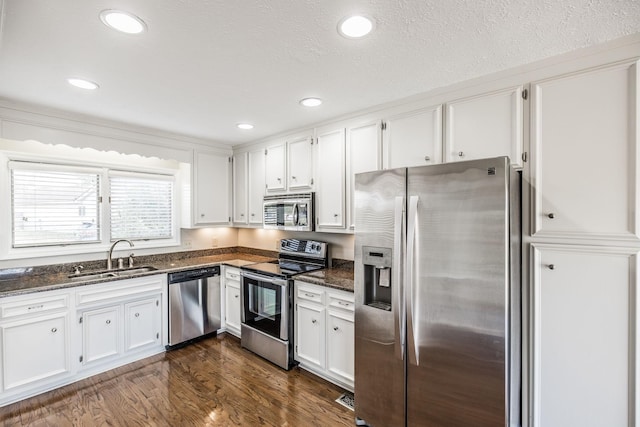 kitchen with white cabinetry, appliances with stainless steel finishes, sink, and dark stone counters