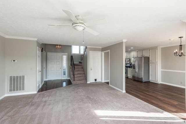 unfurnished living room with dark colored carpet, ornamental molding, ceiling fan with notable chandelier, and a textured ceiling