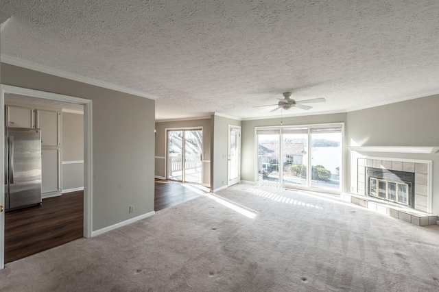 unfurnished living room featuring carpet floors, a tiled fireplace, ornamental molding, ceiling fan, and a textured ceiling