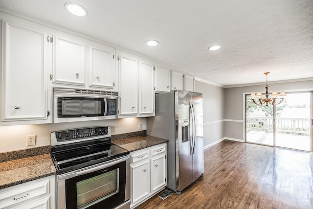 kitchen featuring crown molding, appliances with stainless steel finishes, hanging light fixtures, white cabinets, and dark stone counters