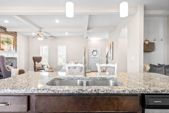 kitchen with sink, beam ceiling, decorative light fixtures, dishwasher, and a fireplace