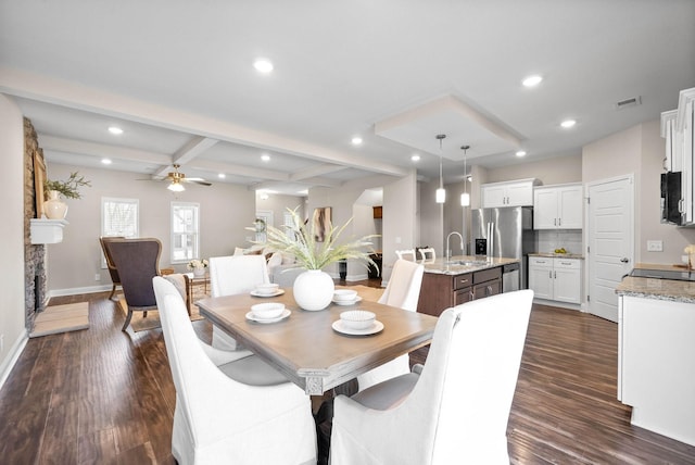 dining area with sink, ceiling fan, a fireplace, dark hardwood / wood-style flooring, and beamed ceiling