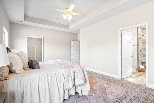 carpeted bedroom featuring a raised ceiling, connected bathroom, and ceiling fan