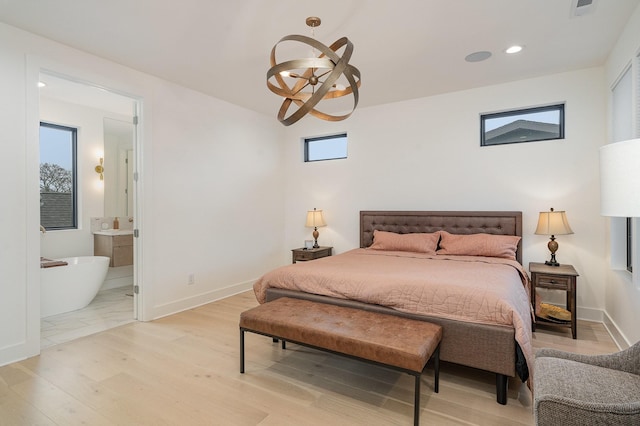 bedroom with ensuite bathroom, an inviting chandelier, and light wood-type flooring