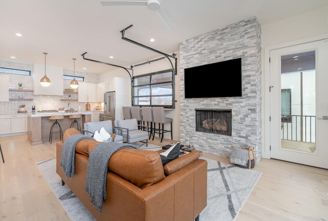 living room featuring sink, a stone fireplace, light hardwood / wood-style floors, and ceiling fan