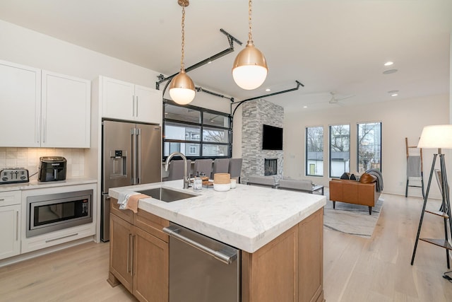 kitchen with stainless steel appliances, a fireplace, an island with sink, white cabinets, and decorative light fixtures