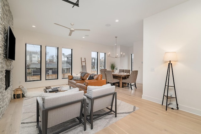 living room featuring ceiling fan with notable chandelier, a fireplace, and light hardwood / wood-style floors