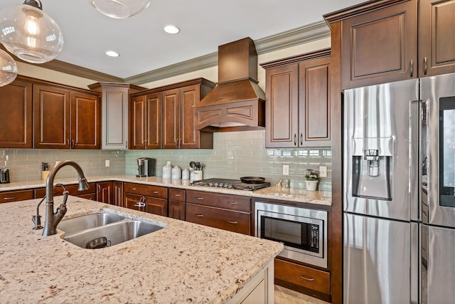 kitchen with sink, appliances with stainless steel finishes, hanging light fixtures, light stone counters, and custom exhaust hood