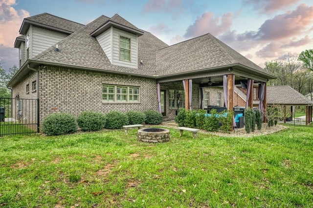 back house at dusk with a lawn, ceiling fan, and an outdoor fire pit