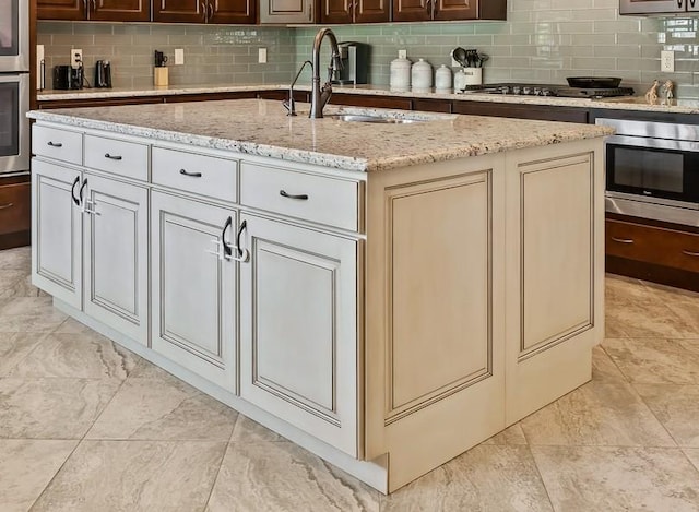 kitchen featuring tasteful backsplash, an island with sink, appliances with stainless steel finishes, and sink