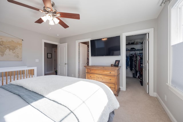 bedroom with light colored carpet, a ceiling fan, baseboards, a closet, and a walk in closet