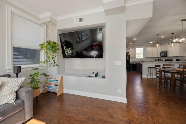 living area featuring crown molding, dark wood-type flooring, visible vents, baseboards, and an inviting chandelier