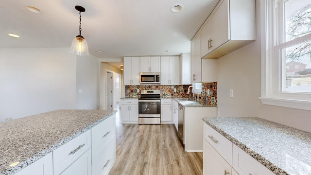 kitchen with white cabinetry, stainless steel appliances, decorative light fixtures, and light stone counters