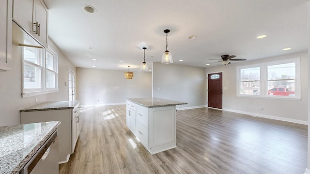 kitchen featuring white cabinetry, hanging light fixtures, a kitchen island, light stone countertops, and light hardwood / wood-style floors