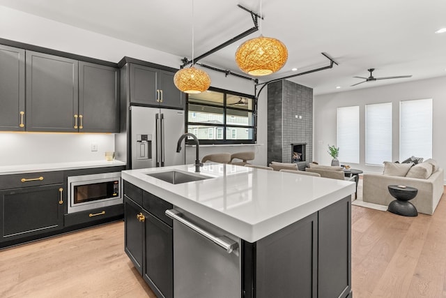 kitchen featuring decorative light fixtures, an island with sink, sink, stainless steel appliances, and a brick fireplace