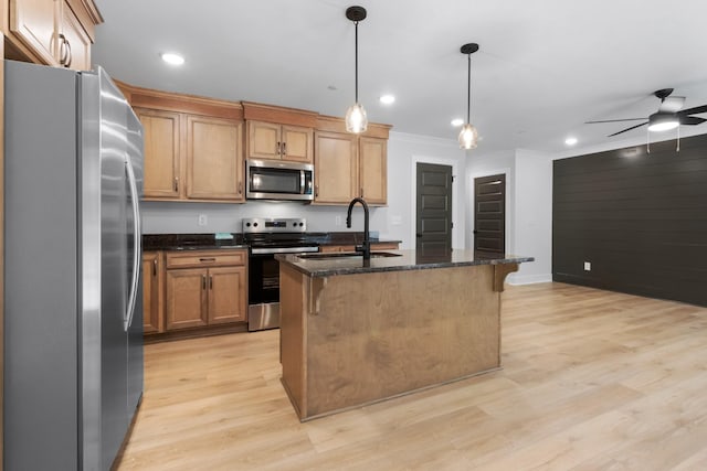 kitchen featuring sink, hanging light fixtures, stainless steel appliances, an island with sink, and dark stone counters