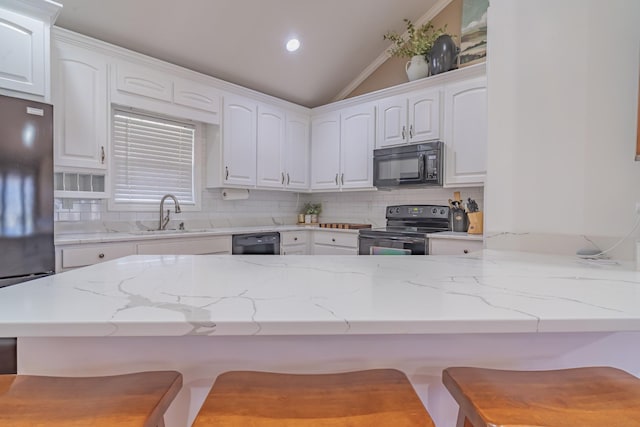 kitchen with vaulted ceiling, sink, a breakfast bar area, white cabinets, and black appliances