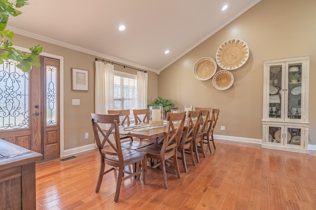 dining area featuring crown molding, lofted ceiling, and light wood-type flooring