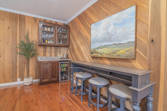 bar featuring wine cooler, ornamental molding, light wood-type flooring, and wood walls