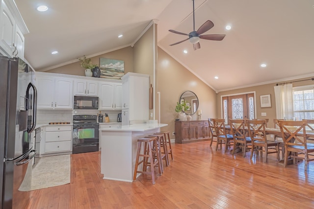 kitchen featuring crown molding, a breakfast bar, black appliances, white cabinets, and decorative backsplash