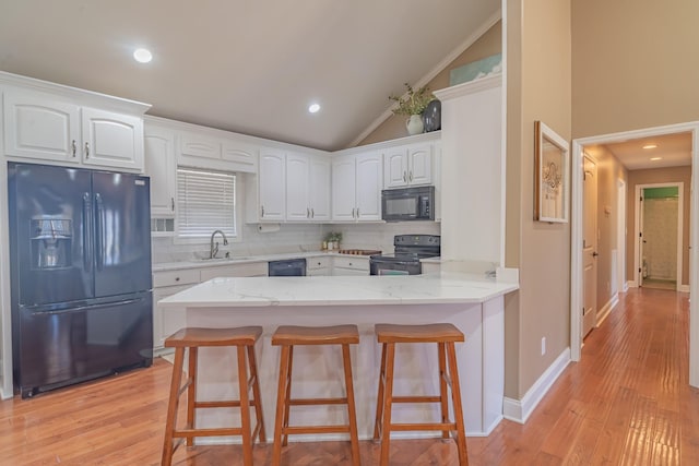 kitchen featuring white cabinetry, tasteful backsplash, black appliances, vaulted ceiling, and kitchen peninsula