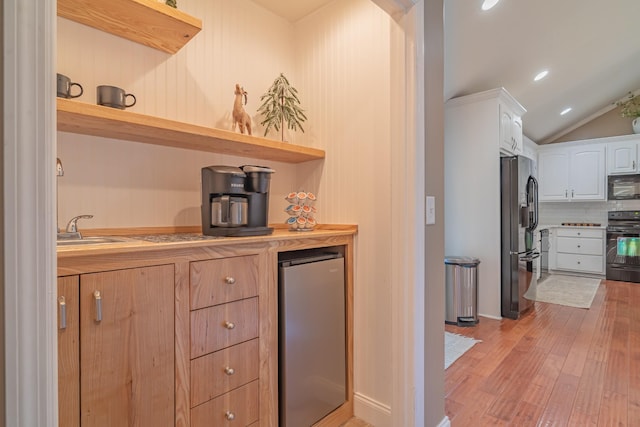 kitchen with butcher block countertops, white cabinetry, vaulted ceiling, light hardwood / wood-style floors, and black appliances