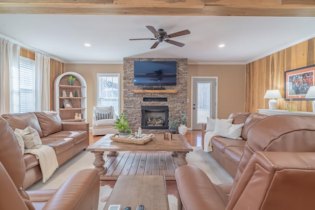 living room with a stone fireplace, ornamental molding, light hardwood / wood-style floors, and ceiling fan