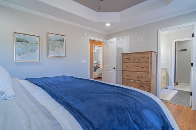 bedroom with hardwood / wood-style flooring, ornamental molding, a tray ceiling, and connected bathroom