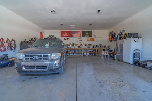 garage featuring stainless steel refrigerator with ice dispenser, white fridge, and a workshop area