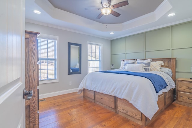 bedroom with ornamental molding, wood-type flooring, ceiling fan, and a tray ceiling