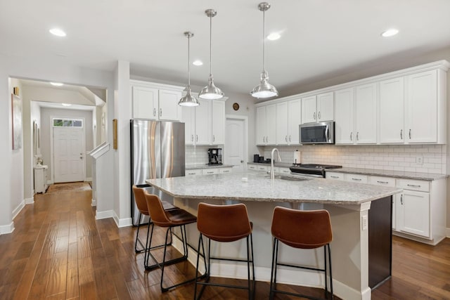 kitchen featuring a center island with sink, appliances with stainless steel finishes, pendant lighting, light stone countertops, and white cabinets