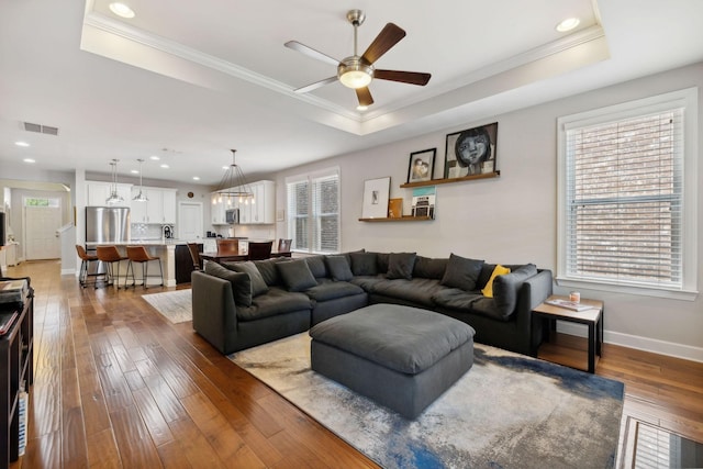 living room featuring dark wood-type flooring, ceiling fan, a tray ceiling, and crown molding