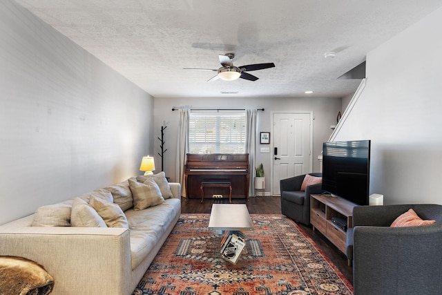 living room featuring ceiling fan, dark wood-type flooring, and a textured ceiling