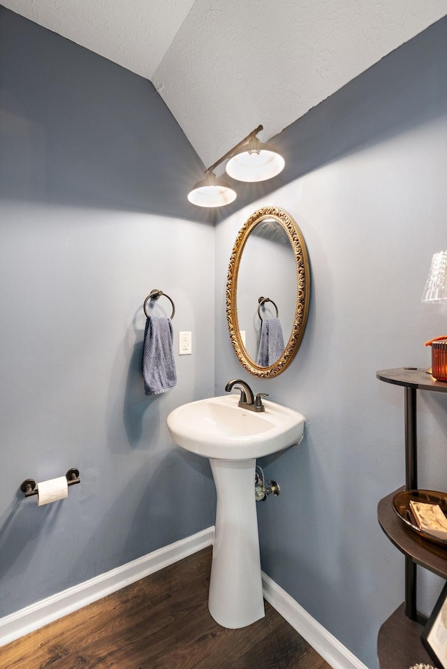 bathroom featuring hardwood / wood-style flooring, vaulted ceiling, and a textured ceiling