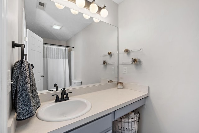 bathroom with vanity, toilet, curtained shower, and a textured ceiling