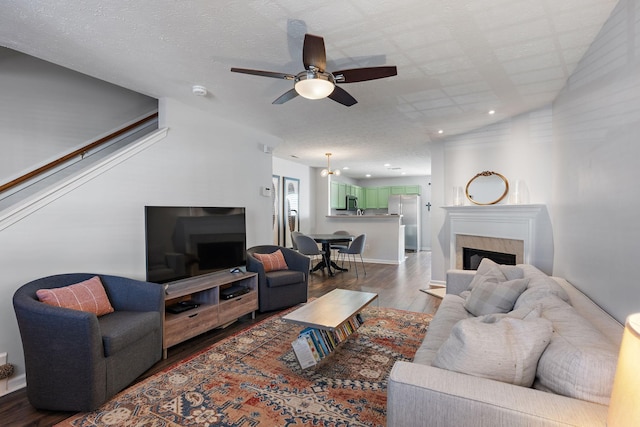 living room with ceiling fan, wood-type flooring, a premium fireplace, and a textured ceiling