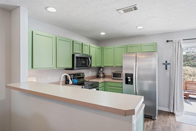 kitchen with appliances with stainless steel finishes, green cabinets, a textured ceiling, and kitchen peninsula