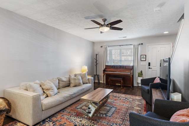 living room featuring ceiling fan, dark wood-type flooring, and a textured ceiling