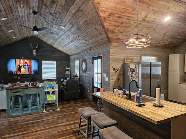 bar featuring dark wood-type flooring, lofted ceiling, wooden counters, stainless steel refrigerator, and wooden walls