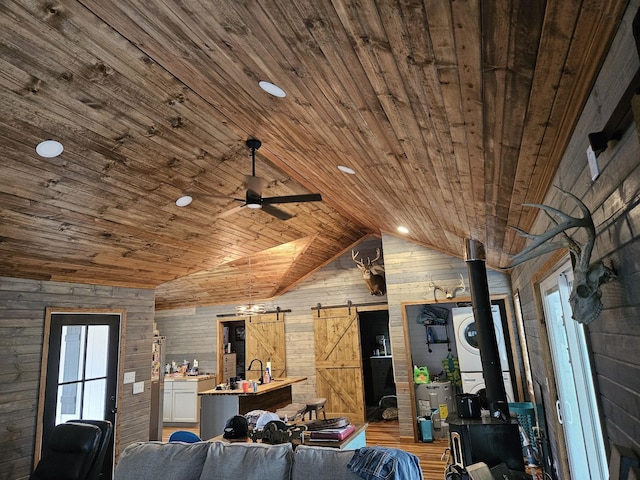 unfurnished living room featuring lofted ceiling, wood ceiling, wooden walls, stacked washer / dryer, and a barn door