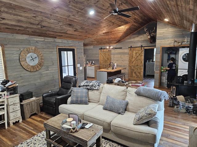 living room featuring stacked washer and dryer, wood-type flooring, wooden ceiling, a barn door, and wood walls