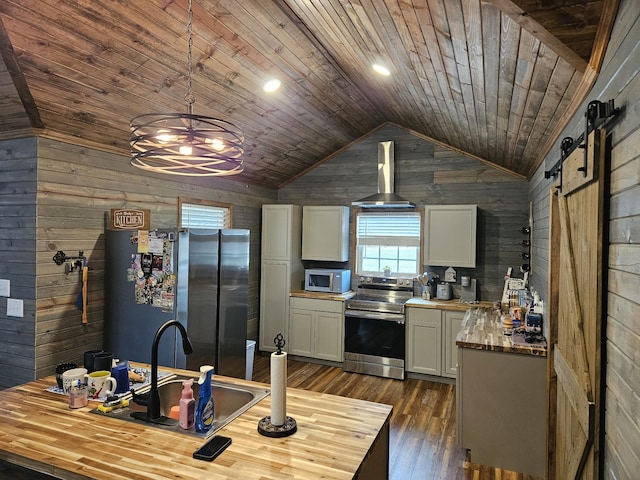 kitchen with hanging light fixtures, stainless steel appliances, a barn door, and wood walls