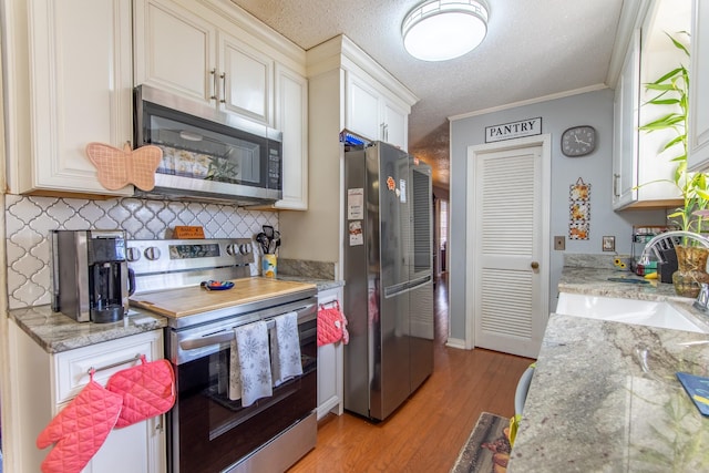 kitchen featuring sink, ornamental molding, stainless steel appliances, a textured ceiling, and light hardwood / wood-style flooring