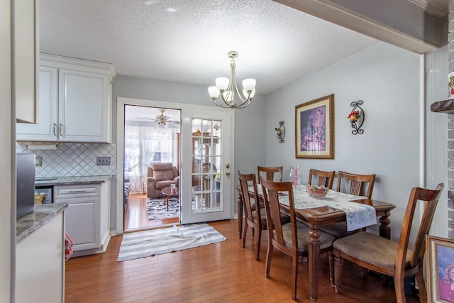 dining room featuring ceiling fan with notable chandelier, a textured ceiling, and light wood-type flooring