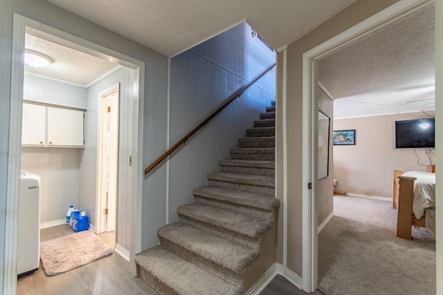 stairway with crown molding, wood walls, a textured ceiling, and carpet flooring