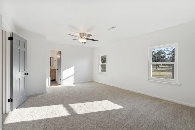 unfurnished bedroom featuring multiple windows, connected bathroom, light carpet, and ceiling fan