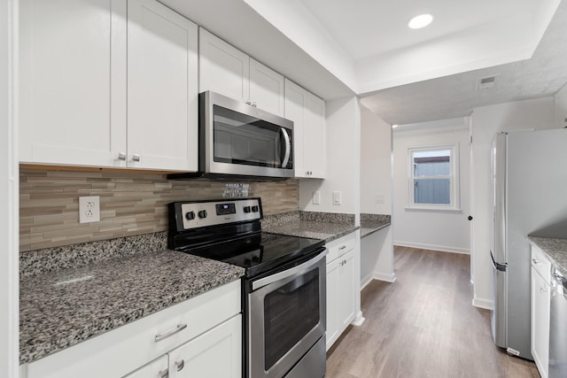 kitchen with tasteful backsplash, white cabinetry, dark stone countertops, stainless steel appliances, and light wood-type flooring