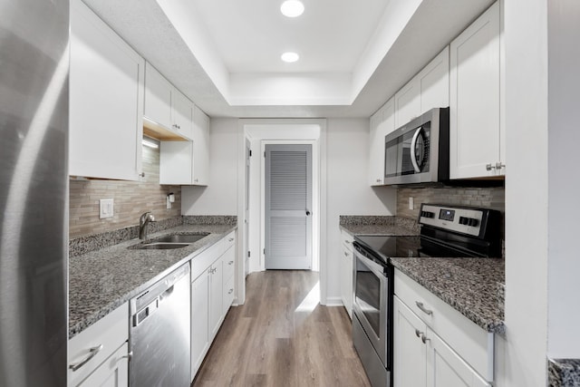 kitchen featuring sink, hardwood / wood-style flooring, appliances with stainless steel finishes, white cabinets, and dark stone counters